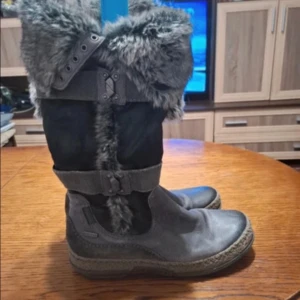 Grå boots med pälsdetaljer från Tamaris - Säljer ett par grå boots med pälsdetaljer och spännen från Tamaris. Supermysiga nu på vintern och till våren! Skorna är köpta på Vinted men är i bra skick! Ca storlek 39!