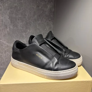 Svarta sneakers från Axel Arigato - Snygga svarta sneakers från Axel Arigato med en stilren design. Skorna har en vit sula och är tillverkade i skinn. Perfekta för en minimalistisk look.