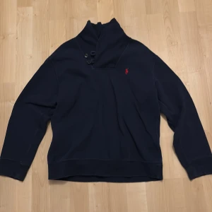 Svart tröja från Polo Ralph Lauren - Säljer en stilren svart tröja från Polo Ralph Lauren med hög krage och knappar. Tröjan är tillverkad i en mjuk bomullsblandning och har långa ärmar. Perfekt för en avslappnad och snygg look. Tröjan är i M(10-12)!