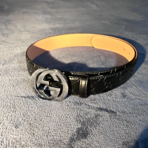 Svart bälte från Gucci med silvrig gucci spänne - Snyggt svart bälte från Gucci med ett stilrent mönster och en iögonfallande silverfärgad spänne. Perfekt för att ge din outfit en lyxig touch. Kommer i originalförpackning.