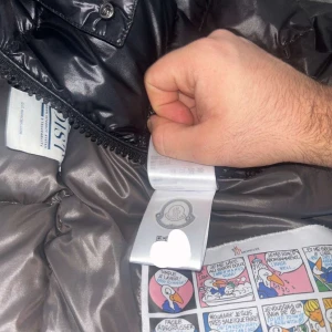 Svart dunjacka från Moncler - Snygg svart dunjacka från Moncler med glansig finish. Jackan har en dragkedja framtill och praktiska fickor. Perfekt för kyliga dagar med sin varma vaddering och stilrena design.