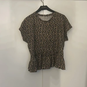 Leopardmönstrad topp från Kappahl - Snygg leopardmönstrad topp från Kappahl med korta ärmar och volangdetalj i nederkant. Perfekt för en trendig look.