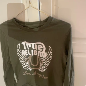 Grön långärmad tröja från True Religion - Snygg grön långärmad tröja från True Religion med tryck i vitt på framsidan. Perfekt för en avslappnad stil med en touch av Los Angeles-vibe.