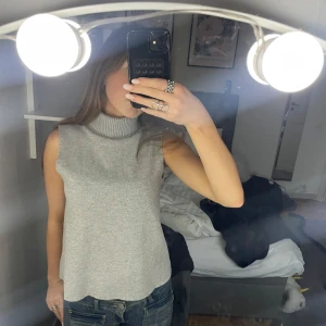 Grå ärmlös polotopp - Snygg grå ärmlös polotopp i mjukt material. Perfekt för lager-på-lager eller att bära som den är. Den har en ribbad polokrage som ger en stilren look.