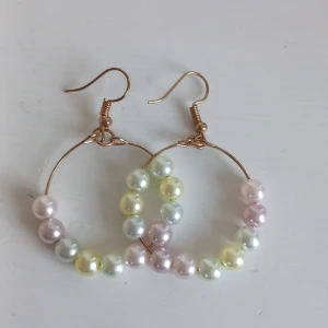Färgglada pärlörhängen - Charmiga örhängen med pärlor i olika pastellfärger som rosa, gul och blå. De är designade i en cirkel med en tunn metalltråd som bas. Perfekta för att ge en färgglad touch till din outfit. Aldrig använda 