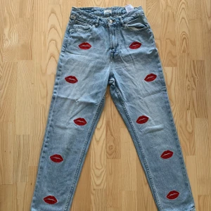 Ljusblå jeans med röda läppmotiv från Q/S - Unika ljusblå jeans från Q/S med coola röda läppmotiv över hela byxorna. De har en klassisk femficksdesign och knappgylf. Priset går att diskutera vid snabb affär. Perfekta för att ge din outfit en rolig och trendig touch. Kontakta gärna mig för fler bilder eller funderingar. 