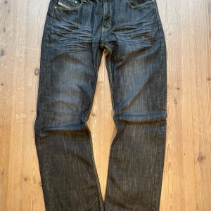 Mörkgråa jeans från Diesel - Snygga mörkgråa jeans från Diesel med kontrasterande gul söm. Klassisk femficksdesign med en läderpatch baktill. Perfekta för en stilren look. De är vintage så har härligt slitage på sig. 