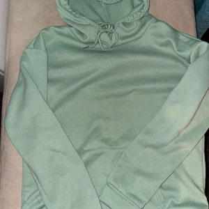 Grön hoodie med blommönster - Säljer en stilren grön hoodie med ett vackert blommönster på ryggen. Tröjan har en justerbar huva med dragsko och långa ärmar. Perfekt för en avslappnad stil. Tunnare material