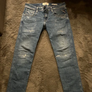 Replay Anbass (NYA) - Snygga blå jeans från Replay med slitna detaljer och en klassisk femficksdesign. De har en slim passform och är perfekta för en avslappnad stil. Märkeslogga på baksidan och dragkedja framtill.  Köptes för 1899kr på pondus.