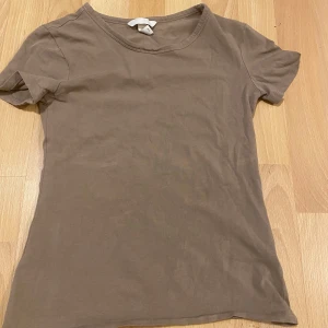 Beige t-shirt från H&M - Säljer en enkel och stilren beige t-shirt från H&M. Den är tillverkad i en mjuk bomullsblandning med 5% elastan för extra komfort. Perfekt basplagg för alla tillfällen.