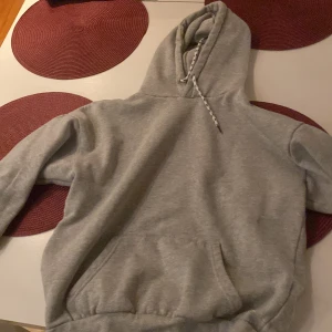Grå hoodie - Säljer en klassisk grå hoodie med justerbar dragsko i huvan och en stor magficka. 