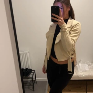 Beige mocka jacka - Snygg beige mocka jacka med dragkedja och bälte. Jackan har en croppad design och passar perfekt för en trendig look. Perfekt för att lyfta vilken outfit som helst! Den är från pretty little thing