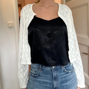 Svart satinlinne - Snyggt svart linne i satin med breda axelband och en elegant v-ringning. Perfekt för en stilren look. Linnet har en slät yta och en bekväm passform.