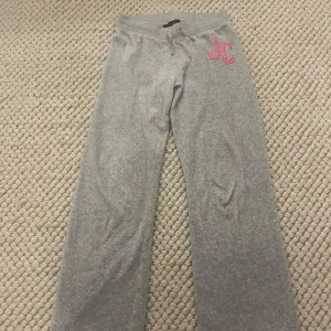 Grå mjukisbyxor från Juicy Couture - Snygga grå mjukisbyxor från Juicy Couture med rosa glittriga JC-bokstäver på. Byxorna har en bekväm passform med ett snöre i midjan och är sparsamt andvända!