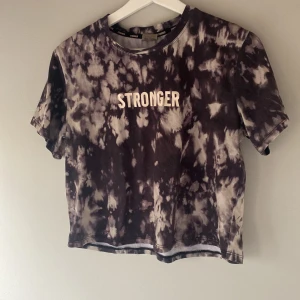 Svart och vit tie-dye t-shirt från Stronger - Säljer en cool svart och vit tie-dye t-shirt från Stronger. T-shirten har korta ärmar och texten 'STRONGER' tryckt på framsidan. Perfekt för en avslappnad stil och för att träna i!