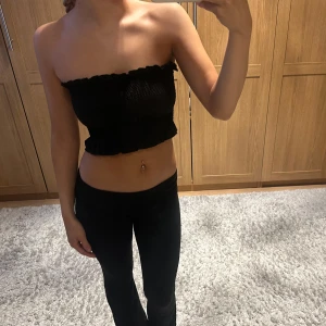Svart tubtopp - Säljer en stilren svart tubtopp med volangdetaljer. Perfekt för en trendig look. Passar bra till både jeans och kjol.