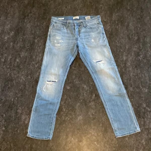 Blå jeans med slitningar - Snygga blå jeans med slitningar och en slim passform. De har en klassisk femficksdesign och en modern look med slitna detaljer. Perfekta för en avslappnad stil. Storlek 31/30