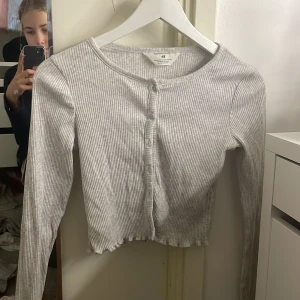 Grå ribbad kofta från H&M - Säljer en stilren grå ribbad kofta från H&M. Den har långa ärmar och knappar framtill. Perfekt för lager-på-lager och passar till många olika outfits. 🩶 helt ny jag har aldrig andvänt 🫶🏻
