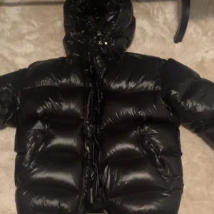 Svart pufferjacka från Zara - Säljer en svart pufferjacka från Zara. Jackan har en glansig finish och är utrustad med en dragkedja framtill. Perfekt för kyliga dagar med sin vadderade design och huva.HAR ANVÄNT DEN 2 GÅNGER.Priset kan diskuteras.storlek M.Köpte för 1,400