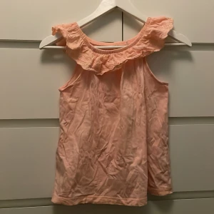 Rosa ärmlös topp med volang - Söt rosa ärmlös topp från Eco med volangdetaljer runt axlarna eller var man än vill ha den. Perfekt för varma dagar och ger en romantisk touch till din outfit. Toppen är i ett mjukt och bekvämt material.