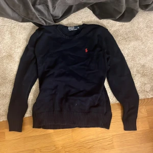 Mörkblå tröja från Polo Ralph Lauren - Säljer en stilren svart tröja från Polo Ralph Lauren med det klassiska röda logotypbroderiet på bröstet. Tröjan är strl M men skulle säga att den sitter mer som en S
