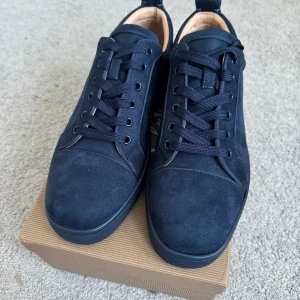 Mörkblå Loubs med röd sula - Snygga mörkblå sneakers i mocka med ikonisk röd sula. Skorna har snörning och en stilren design med broderad logga på hälen. Perfekta för en trendig look.