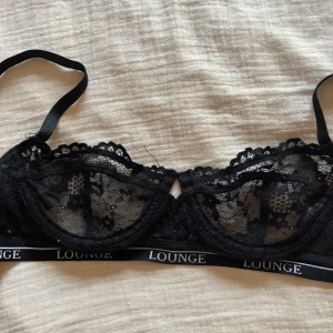 Svart spets-BH från Lounge - Säljer en elegant svart spets-BH från Lounge. Den har justerbara axelband och en elastisk kant med Lounge-loggan. Perfekt för en stilren look.