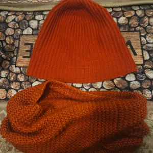 Orange stickad mössa och halsduk från H&M - Säljer en snygg orange stickad mössa och matchande halsduk från H&M. Mössan har en ribbad design som ger en skön passform. Perfekt för att hålla värmen under höst och vinter. Både mössan och halsduken är i en härlig orange färg som lyser upp i mörkret.