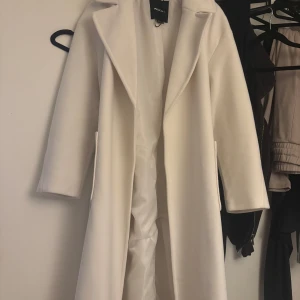 Vit kappa från Pull&bear - Elegant vit kappa från Zara med långärmad design och klassisk krage. Perfekt för en stilren look under kyligare säsonger. Kappan har en tidlös och sofistikerad stil.