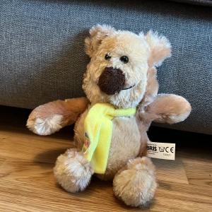 Mjuk nalle med gul halsduk - Söt och mjuk nallebjörn från BRIS med en ljusbrun päls och en gul halsduk. Perfekt som en kramgo vän eller som en fin present. Tillverkad av 100% polyester.