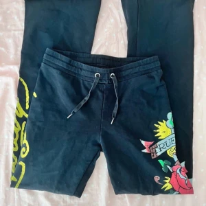 Svarta mjukisbyxor med tryck från Ed Hardy - Snygga svarta mjukisbyxor från Ed Hardy med färgglatt tryck av rosor och texten 'True Love'. Byxorna har en bekväm resårmidja med snörning och unika detaljer i gult och rött.