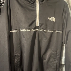 Svart jacka från The North Face - Snygg svart jacka från The North Face med dragkedja och broderad logga på bröstet. Jackan har långa ärmar och en stilren design med märkets namn längs bröstet.