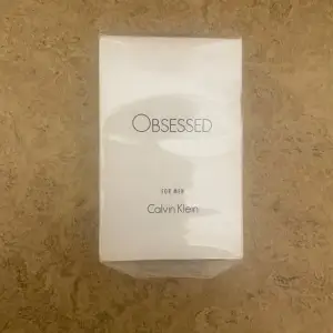 Säljer en 30 ml flaska av Obsessed for Men Eau de Toilette från Calvin Klein. Denna parfym har en modern och maskulin doftprofil. Förpackningen är elegant och stilren i vitt med svart text.