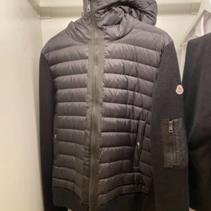 Svart jacka från Moncler - Säljer en snygg svart jacka från Moncler i mycket bra skick. Den har en quiltad framsida med dragkedja och en huva för extra värme. Ärmarna är långärmade och stickade, vilket ger en cool kontrast. Perfekt för höst och vinter! 🖤