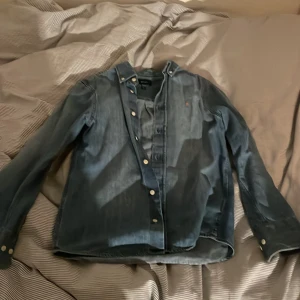 Blå jeansskjorta från GANT - Säljer en snygg blå jeansskjorta från GANT i bra skick. Skjortan har långa ärmar och knappar framtill. Perfekt för både vardag och lite finare tillfällen. Den är tillverkad i ett slitstarkt material och har en broderad logga på bröstet. Passar perfekt för höst och vår!