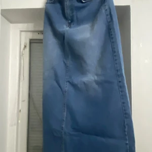 Blå jeanskjol med fransad kant - Snygg blå jeanskjol med fransad kant och klassisk femficksdesign. Kjolen har en rak passform och är perfekt för en avslappnad stil. Den har bälteshällor och en knappstängning framtill. Den är storlek S men passar även XS och M. Längde är ungefär 103cm