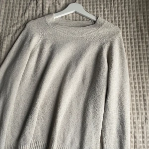 Beige stickad tröja från Vero Moda - Mysig beige stickad tröja från Vero Moda. Perfekt för kyliga dagar med sin klassiska design och bekväma passform. Tröjan har långa ärmar och ribbade detaljer vid hals och ärmslut.