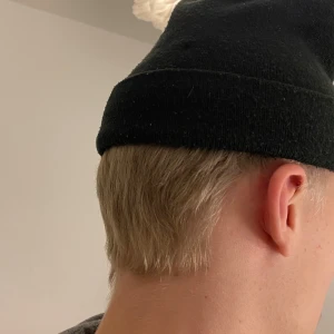 Svart mössa från Lyle & Scott - Snygg svart mössa från Lyle & Scott med deras ikoniska gula logga framtill. Perfekt för att hålla värmen under kalla dagar. Den är i one size och passar de flesta. Stilren och enkel design som funkar till alla outfits. 🖤