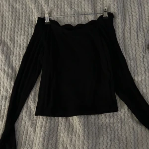 Svart offshoulder topp - Snygg svart offshoulder topp med långa ärmar. Perfekt för en kväll ute eller en fest. Den har en elegant och stilren design som passar till många olika outfits.