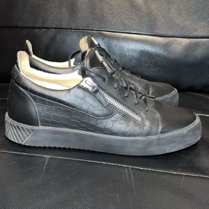 Svarta sneakers med dragkedja - Snygga svarta zanottis sneakers med krokodilmönster och dragkedja på sidan. Skorna har snörning och en robust sula för extra komfort. Perfekta för en stilren look.