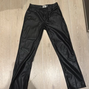 Svarta skinnbyxor från 157 - Snygga svarta skinnbyxor från 157 i storlek S. Byxorna har en klassisk straight passform med knappar och dragkedja framtill. Perfekta för en stilren look.