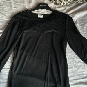 Svart tröja från Jacqueline de Yong - Snygg svart tröja från Jacqueline de Yong i storlek M. Den har ett vackert spetsmönster upptill och trekvartsärmar. Perfekt för både vardag och festliga tillfällen. Klänningen är i mycket bra skick och ger en elegant look.