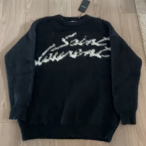  Saint Laurent hoodie - Säljer en snygg svart tröja från Saint Laurent med deras ikoniska logga i vitt på framsidan. Tröjan är i storlek L men sitter lite större skulle jag säga och är perfekt för både vardag och fest. Den är i mycket bra skick och redo för en ny ägare. 