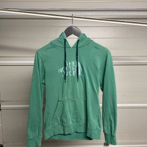 Grön hoodie från The North Face - Säljer en snygg grön hoodie från The North Face. Den har en klassisk känguruficka och justerbar huva med snören. Perfekt för kyliga dagar eller som ett extra lager. Passar både till vardags och för utomhusaktiviteter. Hör av dig vid intresse! Säljes i befintligt skick. Storlek: Kidsize