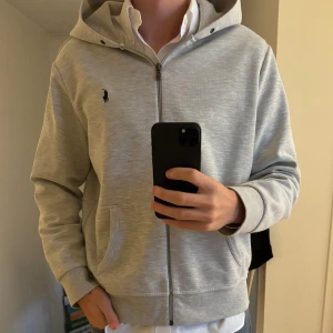 Grå huvtröja från Ralph Lauren - Snygg grå huvtröja från Ralph Lauren med dragkedja och broderad logga på bröstet. Size medium, den är bra skick och passar till massa olika stilar. Priset ej hugget i sten. nypris 2000:- mitt pris 599:-