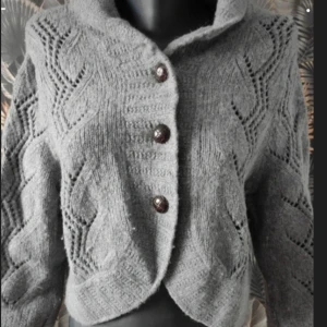 Grå stickad kofta med knappar - Mysig grå stickad kofta med ett snyggt mönster och stora knappar framtill. Perfekt för kyliga dagar och ger en stilren look. Koftan har långa ärmar och en bekväm passform.