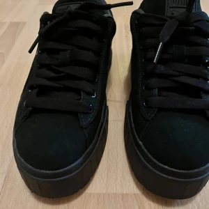 Svarta sneakers från Puma - Säljer ett par snygga svarta sneakers från Puma i mycket bra skick. De har en stilren design med svart mocka och matchande svarta snören. Perfekta för både vardag och fest! 🖤