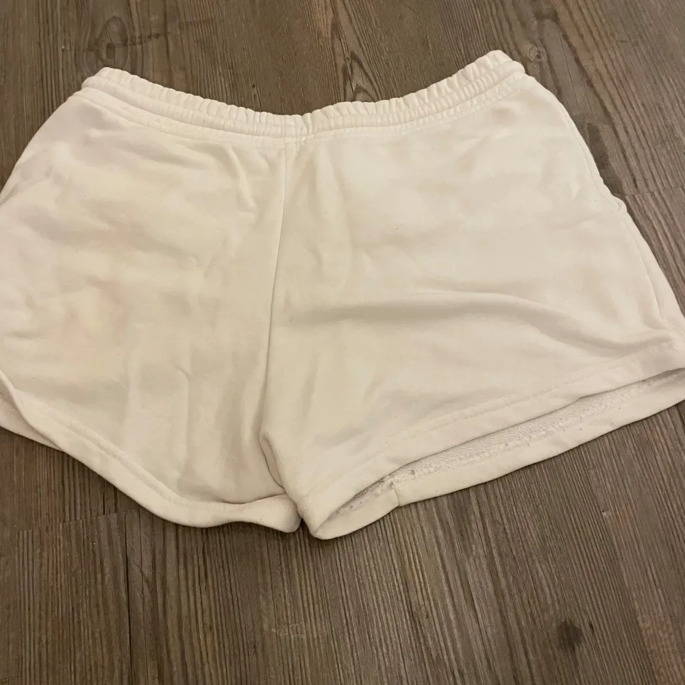 Säljer ett par vita shorts i mjukt material med elastisk midja och dragsko. Perfekta för en avslappnad dag eller träning. De har en bekväm passform och är i bra skick. Fickor på sidorna för extra funktionalitet.. Shorts.