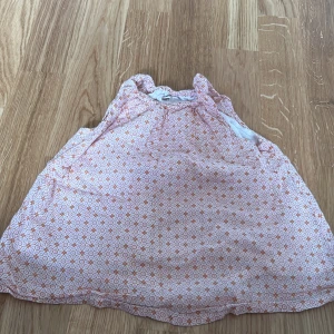 Mönstrad klänning från Lindex - Söt klänning från Lindex med ett orange och vitt geometriskt mönster. Klänningen är ärmlös och har en luftig passform, perfekt för varma dagar. Tillverkad i bomull för en skön känsla mot huden.