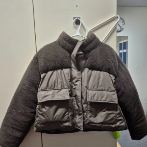 Brun teddyjacka med fickor - Säljer en supermysig brun teddyjacka med stora fickor framtill. Jackan har en cool kombination av teddy och puffer-material, perfekt för höst och vinter. Den är croppad och har en dragkedja framtill. Perfekt för att hålla sig varm och stilren! 🧥✨